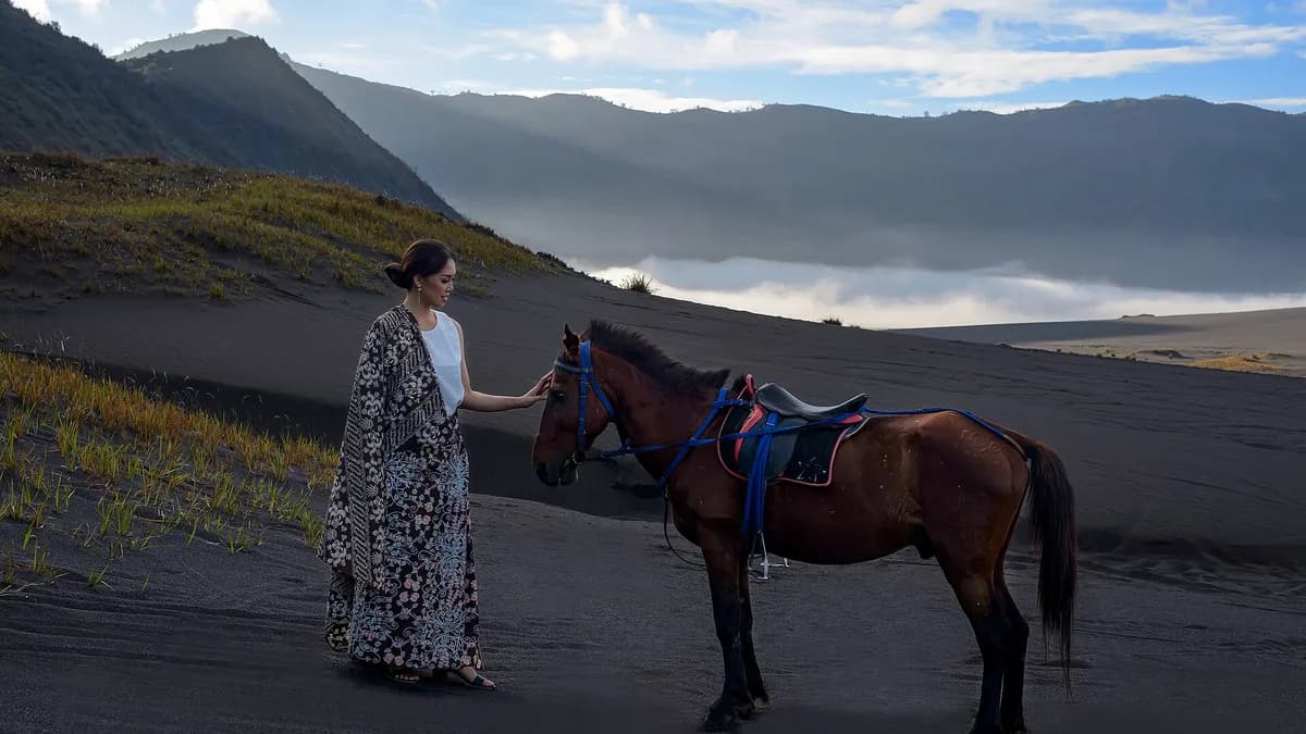 Wisatawan berdiri di samping kuda sewaan di Lautan Pasir Bromo dengan dinding kaldera di latar belakang