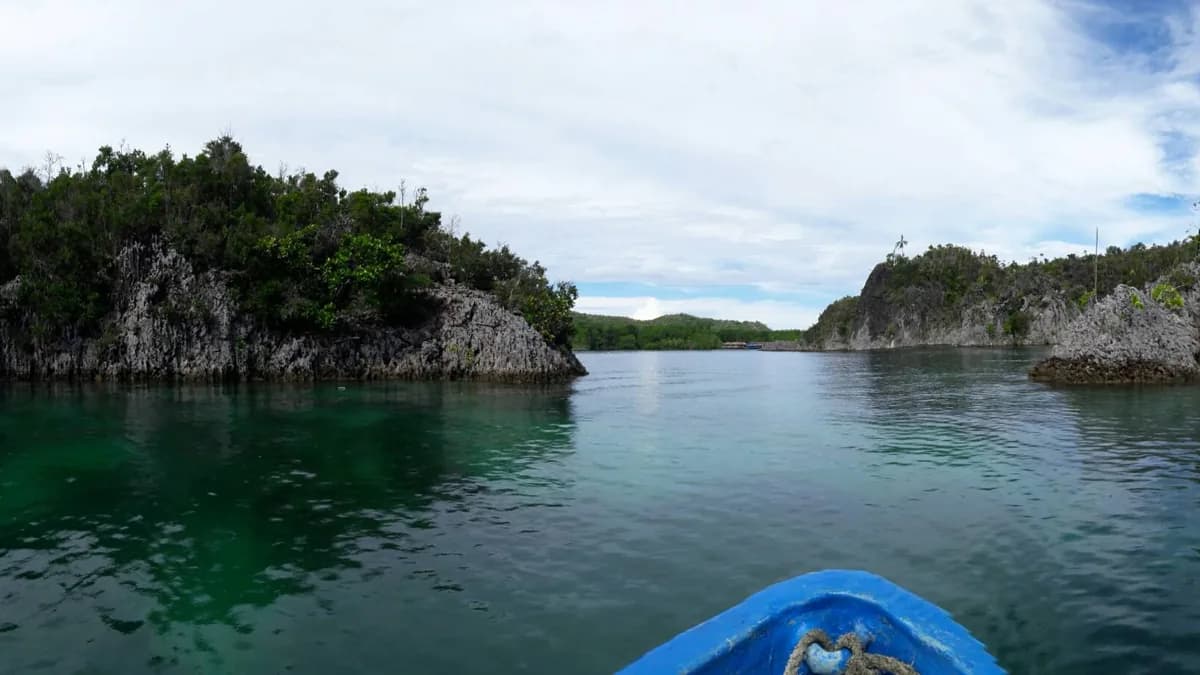 Haluan perahu kayu melintasi selat sempit di antara tebing karst Raja Ampat
