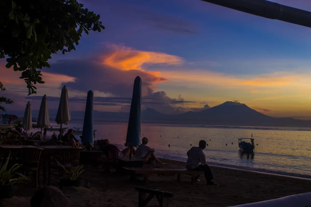 Kursi santai dan payung terlipat di tepi Pantai Sanur dengan siluet Gunung Agung di kejauhan