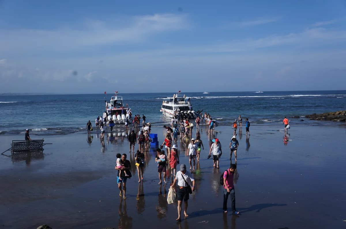 Rombongan wisatawan berjalan di hamparan pasir basah setelah turun dari dua fast boat di Pantai Sanur