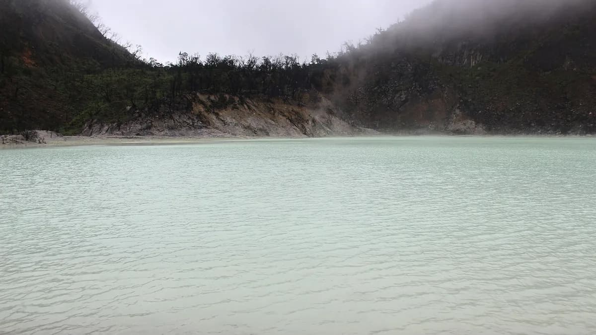Danau kawah Kawah Putih di Ciwidey dengan air putih kehijauan, dinding kawah gelap, dan kabut belerang