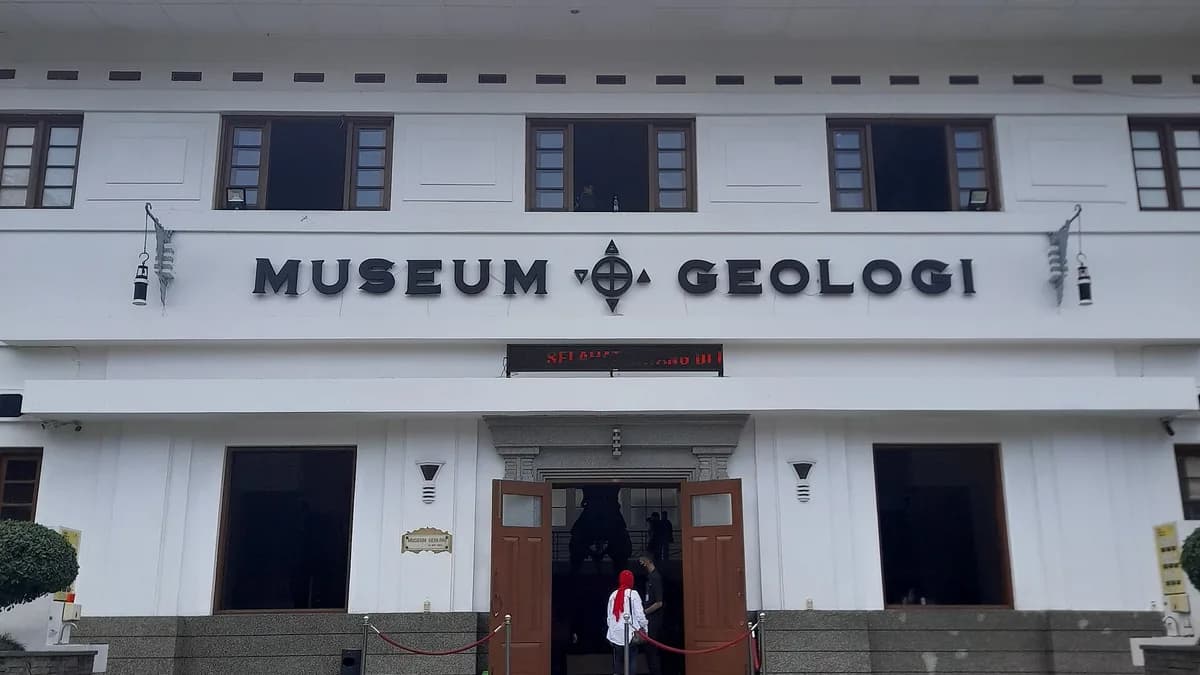 Fasad depan Museum Geologi Bandung berwarna putih dengan huruf timbul MUSEUM GEOLOGI dan pengunjung di pintu masuk