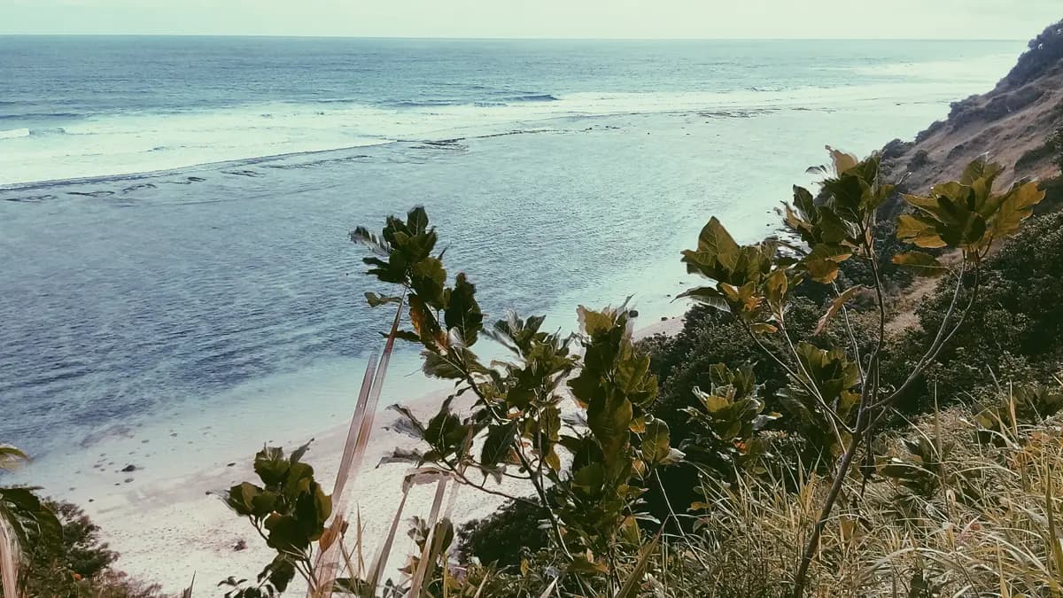 Pantai Gunung Payung dilihat dari jalur di atas tebing, pasir putih sepi dan air toska dangkal