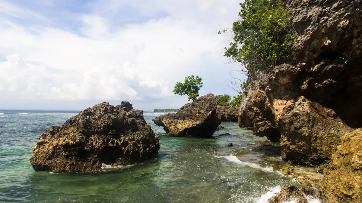 Batu karang besar berdiri di air toska di sisi Pantai Padang Padang, Pecatu, Bali