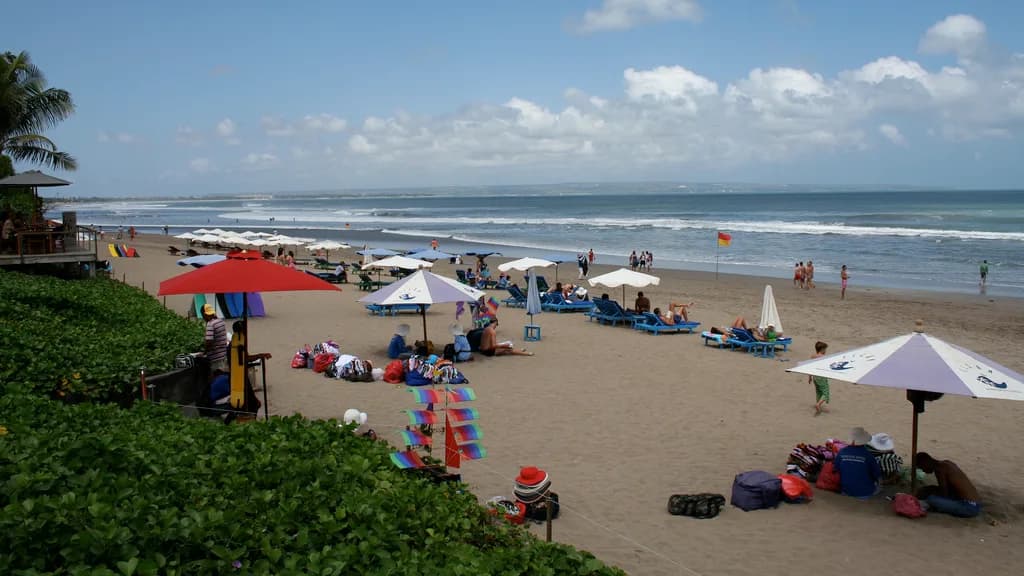 Payung dan kursi pantai berjajar di pasir Pantai Seminyak dengan pengunjung berjemur