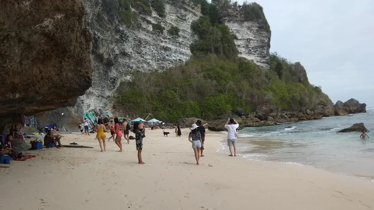 Pengunjung berjalan di pasir Pantai Suluban dengan dinding tebing karang menjulang di belakangnya