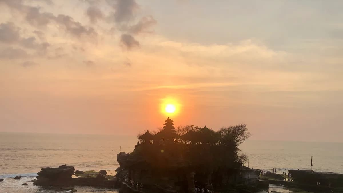 Matahari terbenam tepat di belakang Pura Tanah Lot yang berdiri di atas karang laut