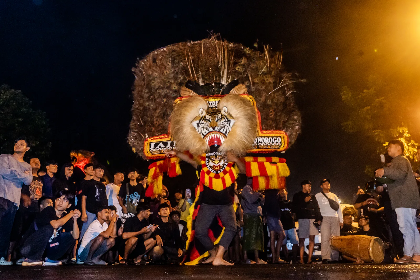 Penari reog memikul dadak merak di tengah jalan pada malam hari dikelilingi kerumunan penonton di depan Alun-Alun Ponorogo