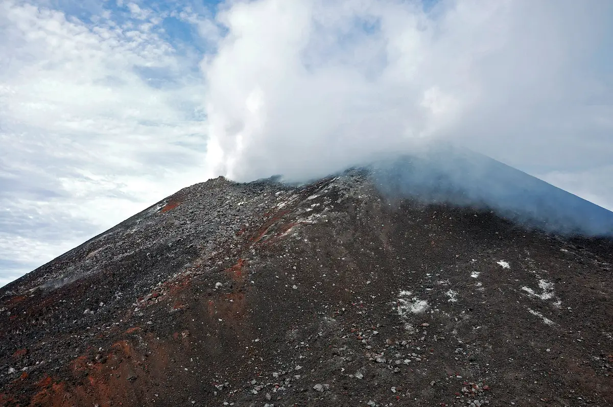 Kerucut Gunung Anak Krakatau berwarna abu gelap dengan asap putih keluar dari puncaknya