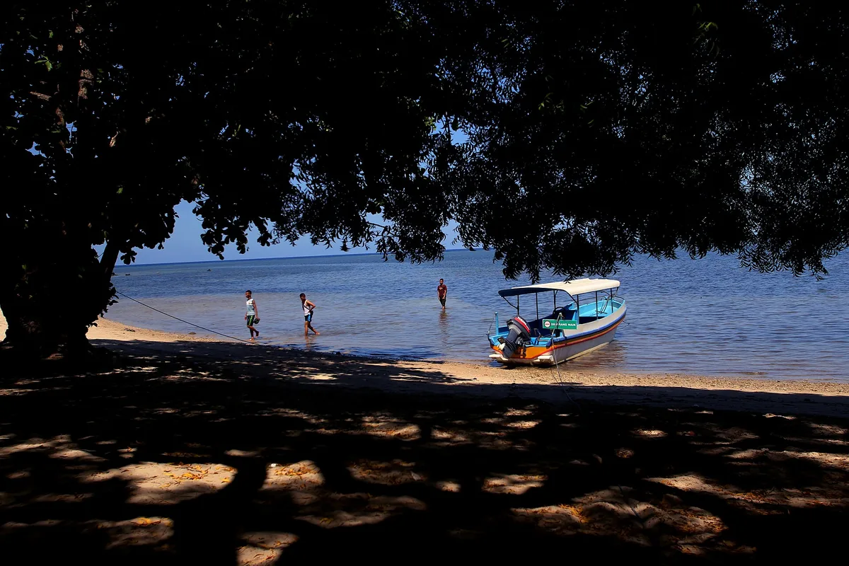 Perahu bersandar di Pantai Bama, Taman Nasional Baluran, dengan pengunjung bermain air di tepi laut