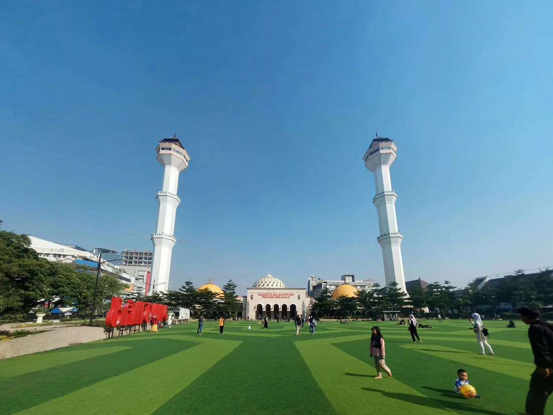 Alun-Alun Bandung berumput sintetis dengan dua menara Masjid Raya Bandung dan pengunjung yang bersantai