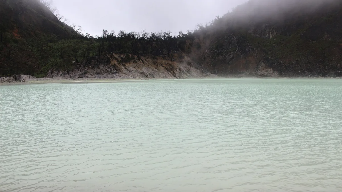 Danau kawah Kawah Putih di Ciwidey dengan air putih kehijauan, dinding kawah gelap, dan kabut belerang
