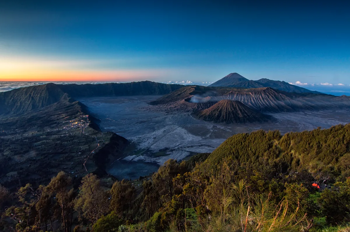 Kaldera Bromo dari Pananjakan 1 dengan Gunung Batok, kawah Bromo berasap, Semeru di kejauhan, dan lampu desa di bibir kaldera