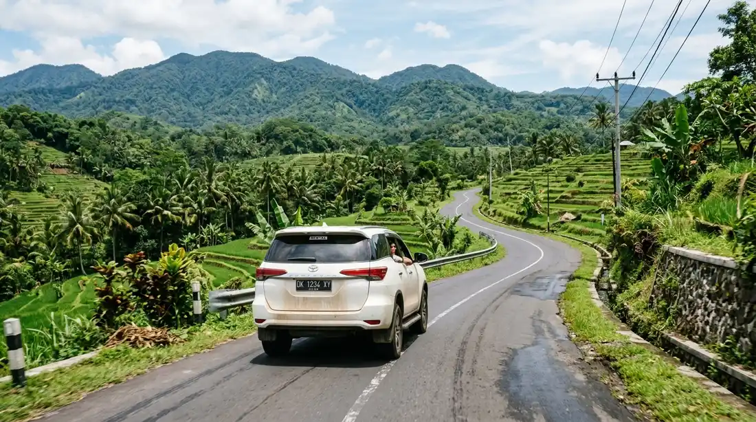 Mobil sewaan melaju di jalan berkelok dengan latar perbukitan hijau