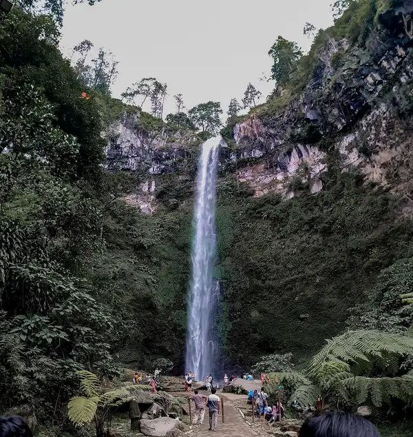 Pengunjung berdiri di area kaki air terjun Coban Rondo yang dikelilingi tebing hijau dan pakis