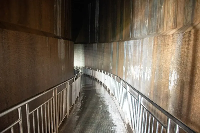 Lorong melengkung berdinding beton tinggi dengan pegangan besi di kedua sisi dan lantai basah di Museum Tsunami Aceh