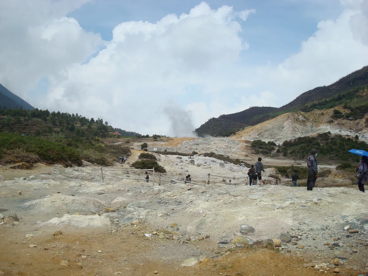 Hamparan belerang dan kepulan uap di Kawah Sikidang, Dieng, dengan pengunjung berjalan di jalur berpagar