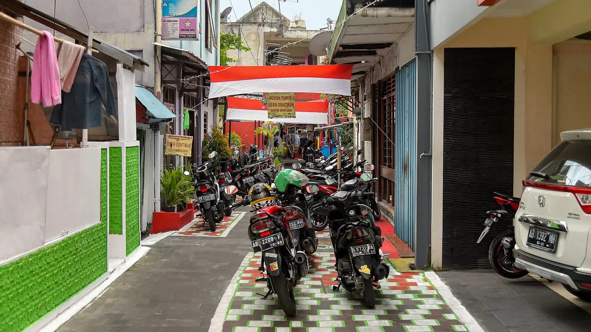 Gang kampung sempit di Yogyakarta dengan deretan sepeda motor terparkir dan jemuran di teras rumah
