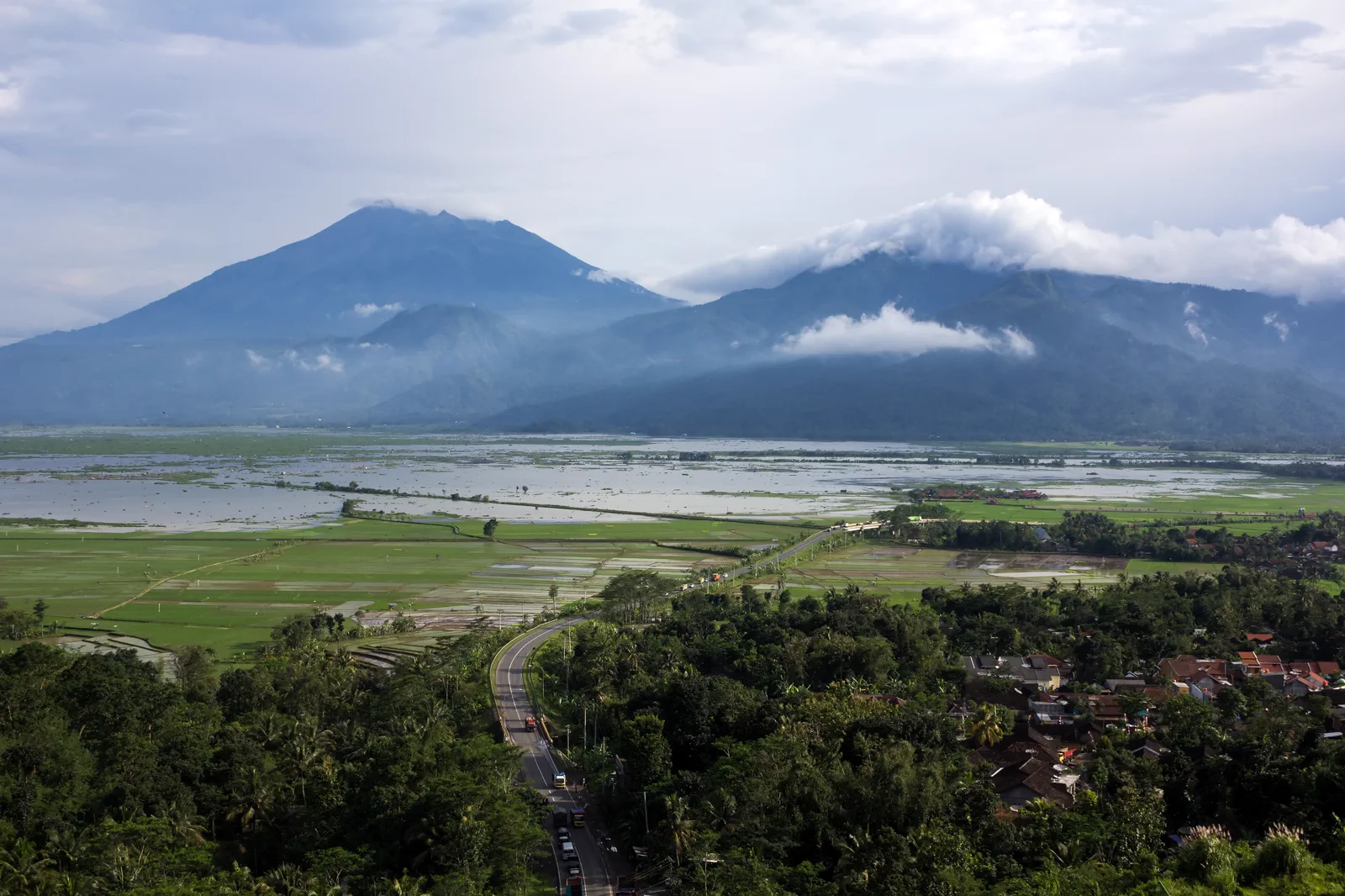 Jalan lingkar Ambarawa membelah persawahan dengan Danau Rawa Pening dan dua puncak gunung di latar belakang