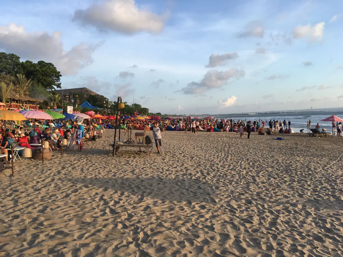Pantai Seminyak menjelang senja dengan payung warna-warni dan pengunjung memadati garis pantai