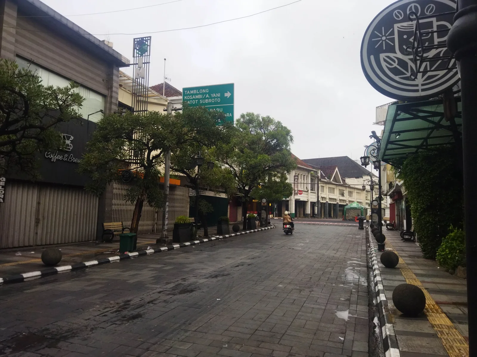 Jalan Braga Bandung pada pagi hari yang basah dengan deretan ruko bergaya art deco dan seorang pengendara motor melintas