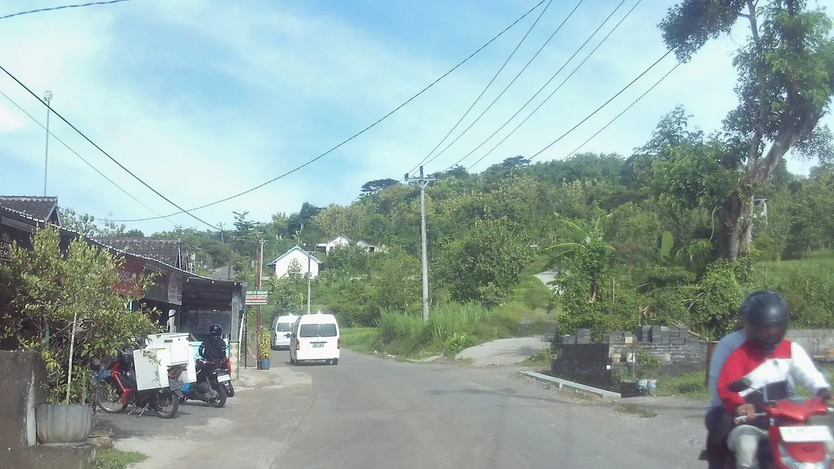 Jalan Candi Ijo di Sleman dengan pengendara motor di bahu jalan dan perbukitan hijau di kejauhan