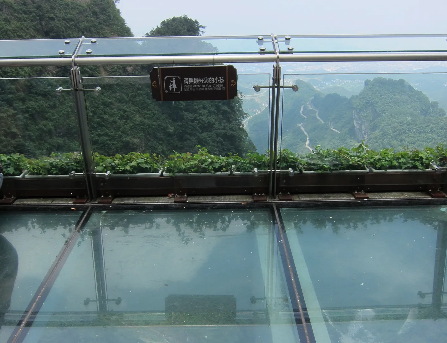 Lantai kaca transparan sebuah jalur skywalk di Gunung Tianmen dengan lembah hijau dan jalan berkelok di baliknya