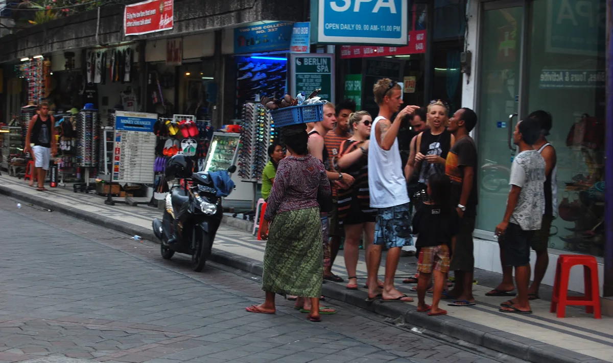 Suasana trotoar Jalan Legian di Kuta dengan wisatawan, kios, dan papan nama spa