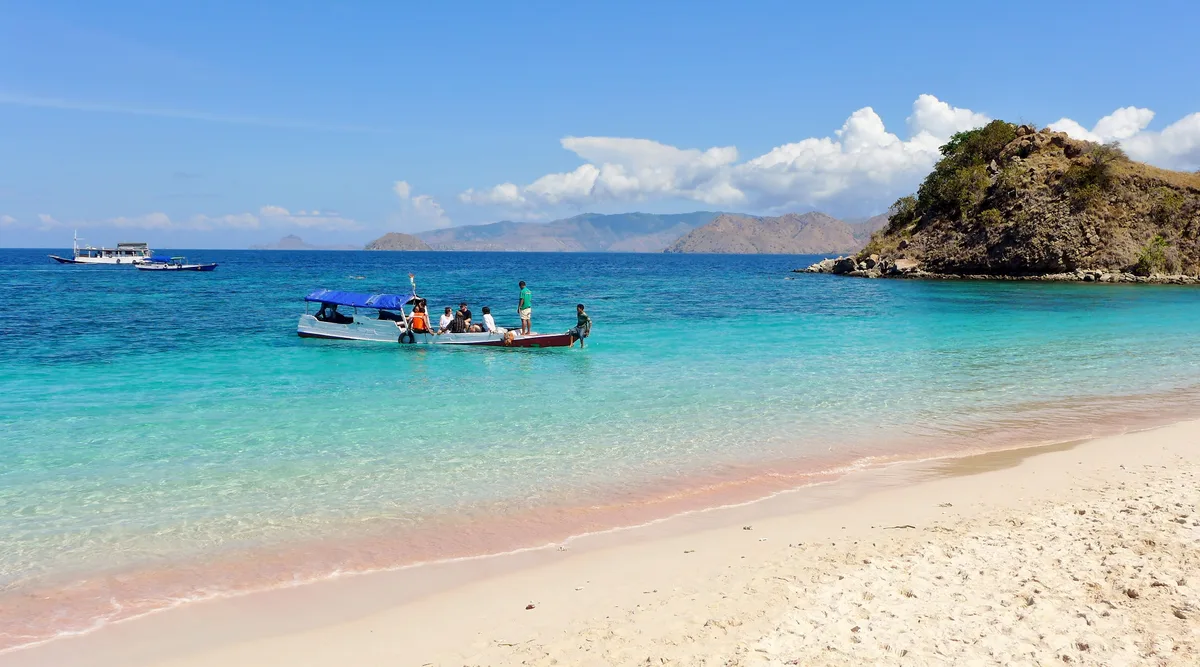 Perahu kayu berpenumpang di perairan jernih Pink Beach, Taman Nasional Komodo