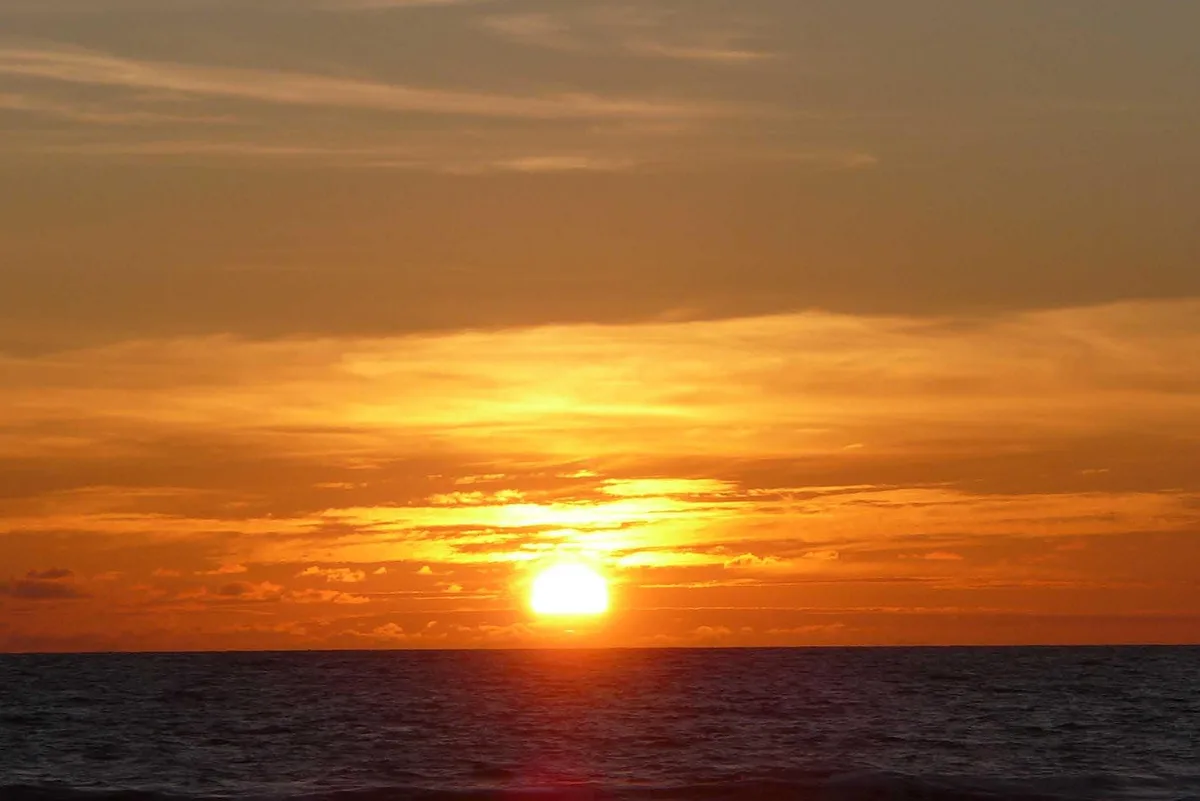 Matahari terbenam di Pantai Legian, Bali, dengan langit jingga dan garis awan gelap di atas laut