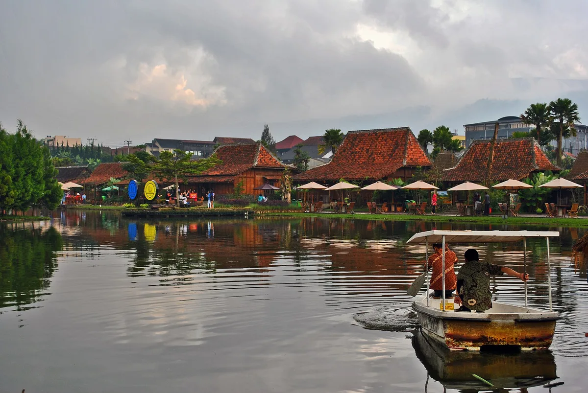 Perahu kayu di danau Floating Market Lembang dengan deretan kios beratap kayu dan payung di tepinya