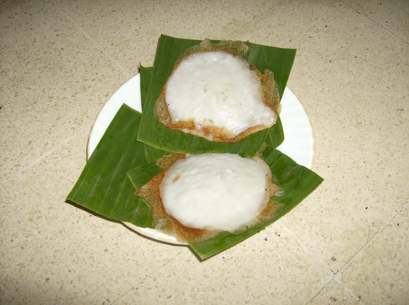 Dua srabi Solo berwarna putih dengan pinggiran kecokelatan disajikan di atas potongan daun pisang di sebuah piring