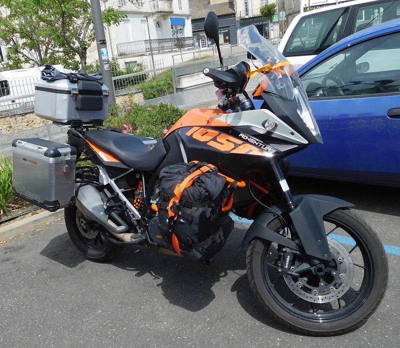 Motor adventure oranye dengan dua boks aluminium di samping dan belakang serta tas bagasi terikat di sisi tangki