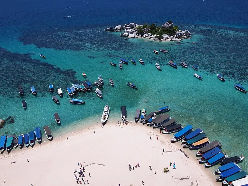 Deretan perahu wisata berlabuh di pantai pasir putih Pulau Lengkuas dengan pulau batu kecil di kejauhan