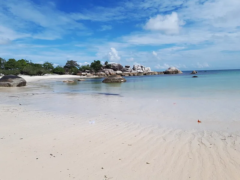 Pantai berpasir putih dengan gugusan batu granit di kejauhan di Pantai Tanjung Tinggi, Belitung