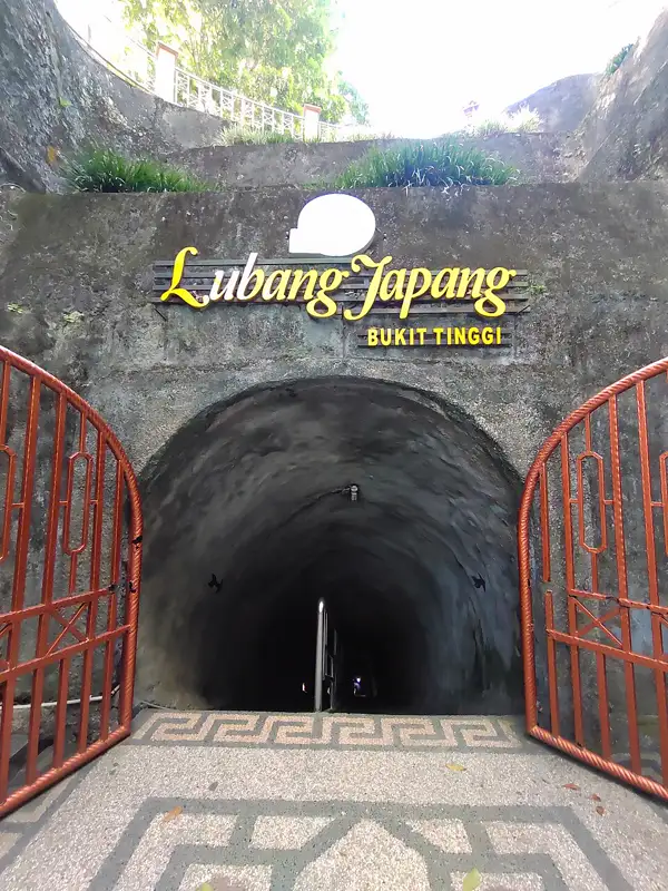 Pintu masuk terowongan Lubang Jepang Bukittinggi dengan gerbang besi oranye dan anak tangga menurun