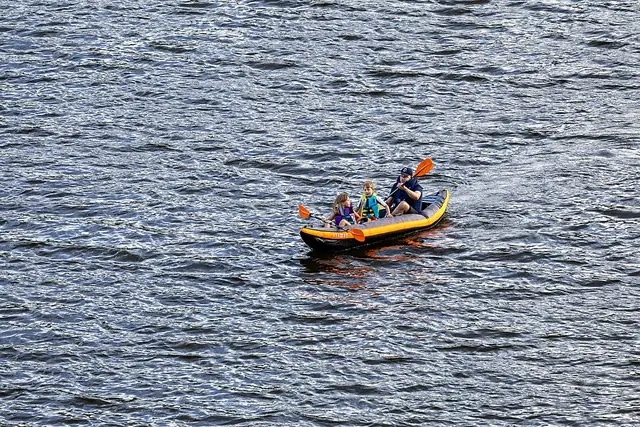 Seorang dewasa dan dua anak berjaket pelampung mendayung kayak tiup di danau
