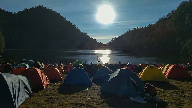 Tenda-tenda di area camping ground Ranu Kumbolo dengan matahari pagi memantul di permukaan danau