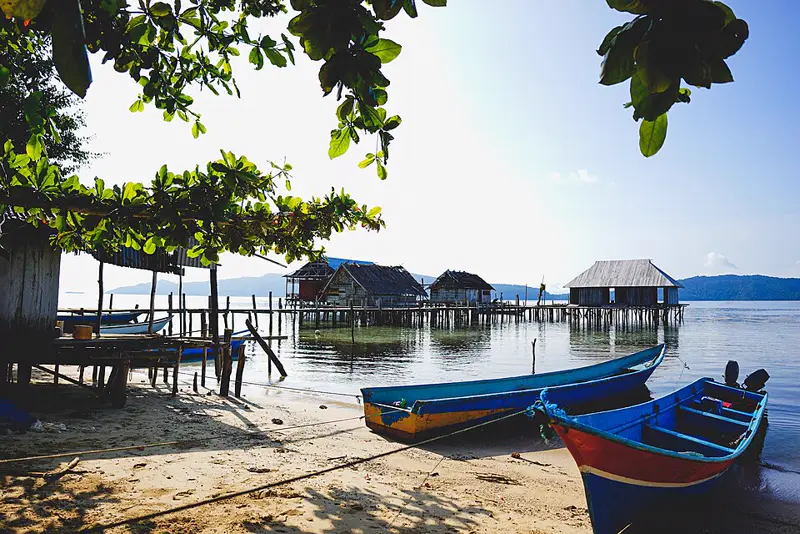 Deretan homestay kayu bertiang di atas air di Kampung Sawinggrai, Raja Ampat, dengan perahu warga di tepi pantai