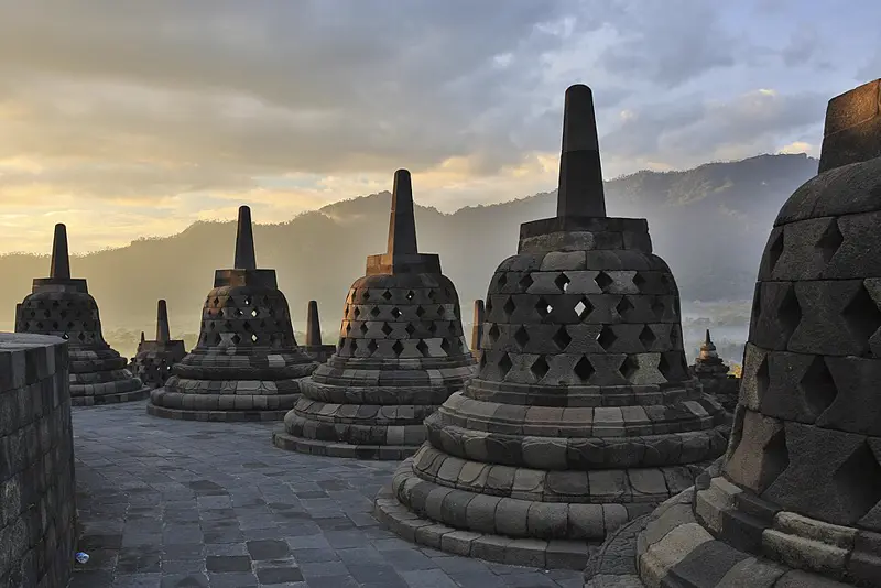 Deretan stupa berlubang berbentuk lonceng di teras atas Candi Borobudur dengan latar perbukitan saat pagi