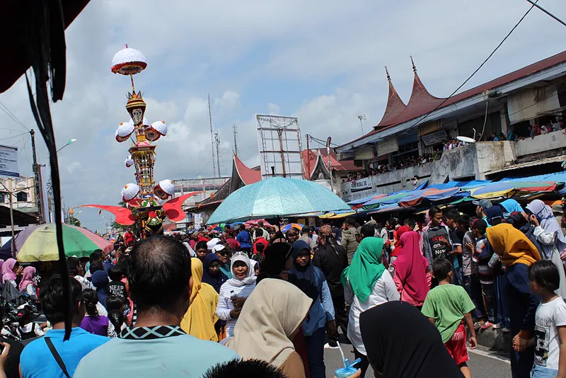 Tabuik bertingkat diarak di jalan Kota Pariaman, dikelilingi kerumunan penonton dan bangunan beratap gonjong