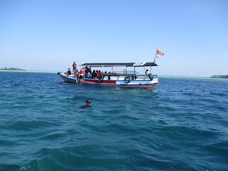 Kapal wisata kayu berisi peserta berpelampung oranye di perairan biru Karimunjawa, seorang peserta snorkeling di dekatnya