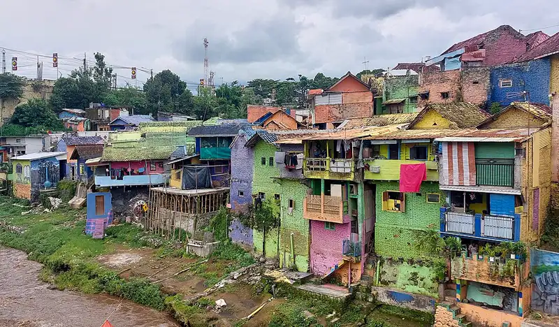 Deretan rumah bertingkat bercat hijau, merah muda, biru, dan kuning di lereng tepi sungai Kampung Warna-Warni Jodipan