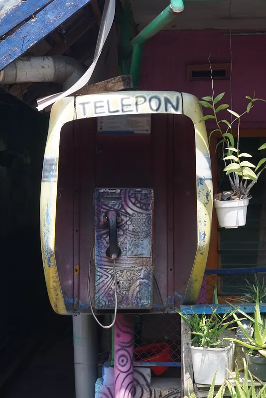 Bilik telepon umum lama berwarna kuning yang dijadikan hiasan dan spot foto di Kampung Warna-Warni Jodipan