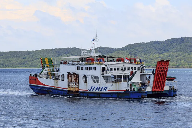 Kapal feri KMP Gilimanuk berlambung biru putih berlayar di Selat Bali dengan perbukitan hijau di latar belakang