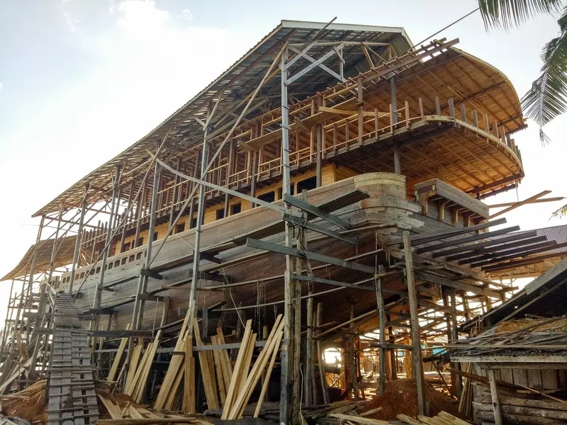 Lambung kayu kapal pinisi yang sedang dibangun dikelilingi perancah di galangan pesisir Tanaberu, Bulukumba