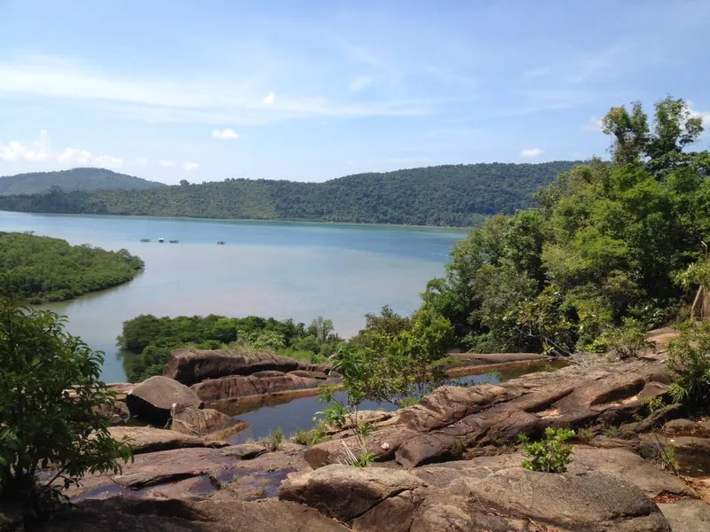 Bebatuan besar di bagian atas Air Terjun Temburun dengan pemandangan teluk dan perbukitan hijau di Kepulauan Anambas