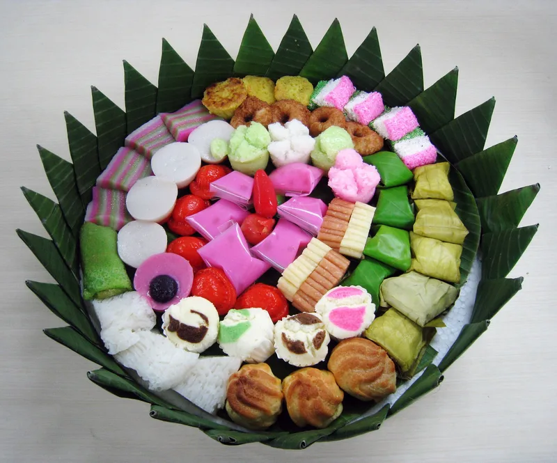 Aneka jajan pasar warna-warni seperti kue lapis, kue ku, dan dadar gulung ditata dalam wadah berhias daun pisang