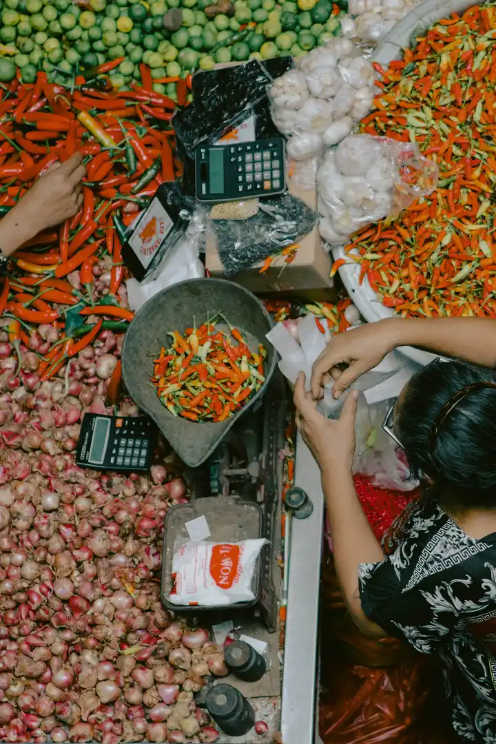 Pedagang menimbang cabai di lapak yang penuh tumpukan cabai, bawang merah, dan bawang putih di Pasar Badung, Denpasar