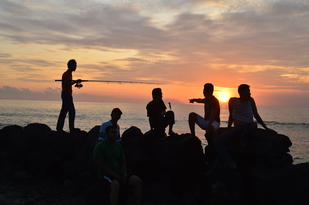 Beberapa orang memancing dari batuan pemecah ombak di Pantai Anyer saat matahari terbenam